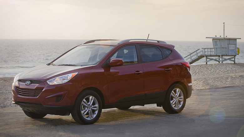 A red 2010 Hyundai Tucson in front of a beach with a lifeguard stand in the background.