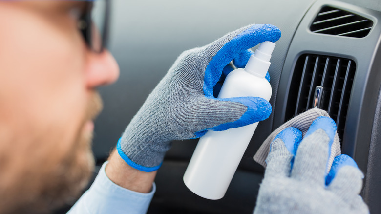 A person cleaning the air vent with a disinfectant spray