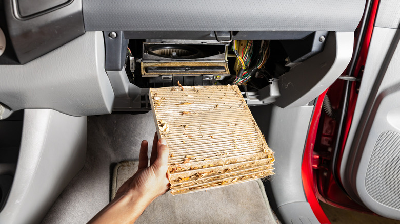 A person removing a disgusting cabin filter from under the dashboard
