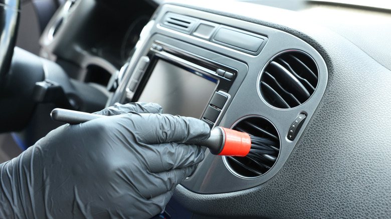 A person cleaning the air vents with a soft detailing brush