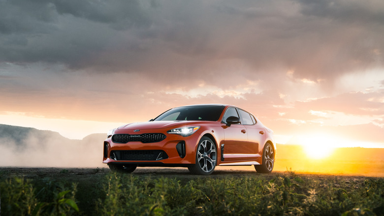 An orange 2019 Kia Stinger GTS parked ahead of a colorful sunset