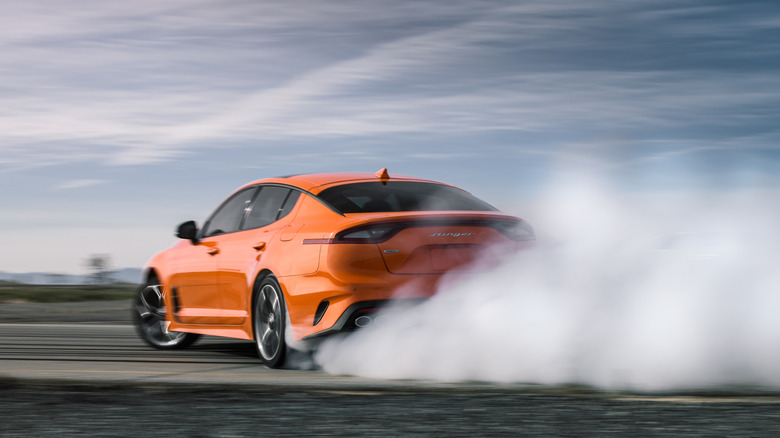 An orange 2019 Kia Stinger GTS kicks up smoke in a slide