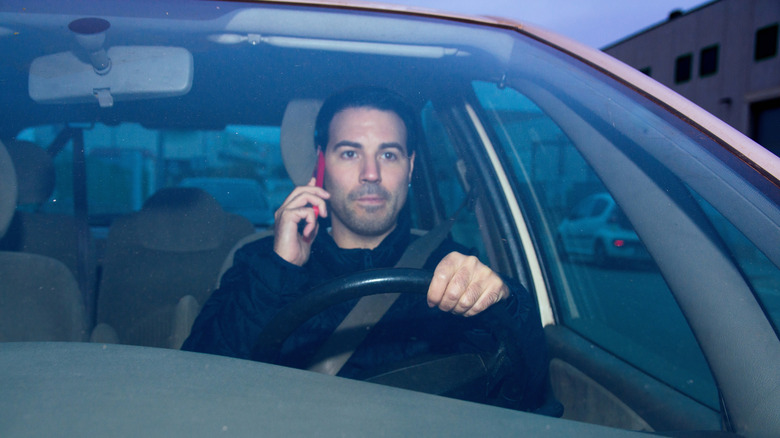 A man driving a car while holding a cell phone up to his ear