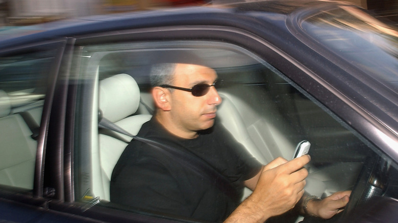 A man writes a text message on his mobile phone whilst driving in traffic on June 24, 2003 in London, England. The government has announced plans for a ban on talking on hand-held mobile phones while driving; this will go into effect by the end of the year.