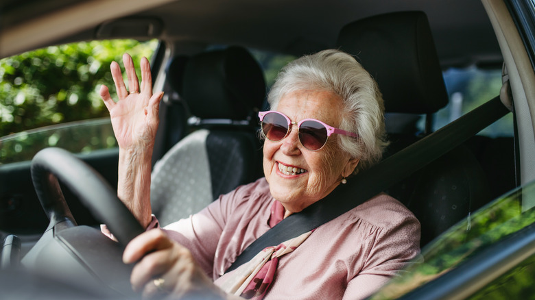 An elderly woman driving a car and waving