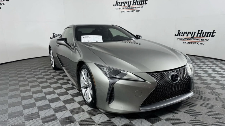 A silver Lexus LC500H parked in a used car show room. The floor is a checkerboard pattern of gray and light gray and the background is white with the words "Jerry Hunt Supercenter Salisbury, NC" in the background