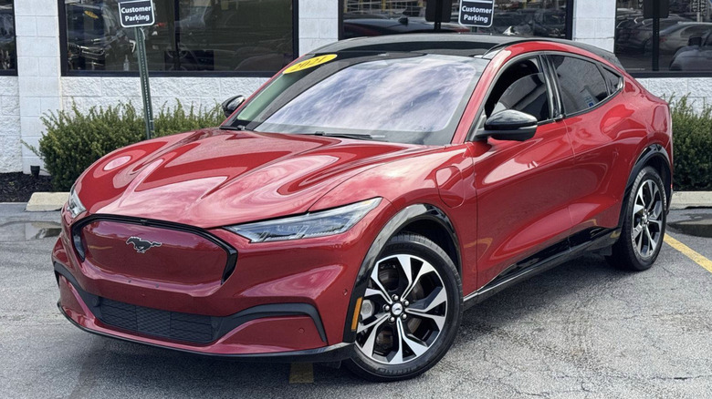 A red Mustang Mach-E parked across several parking spots in front of a used car dealership