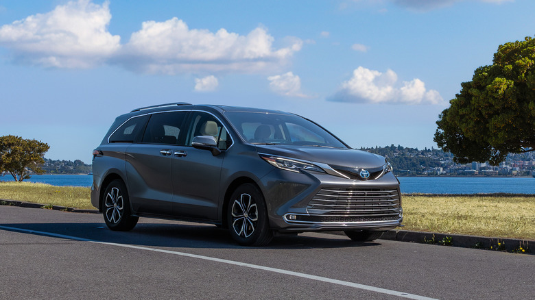 A toyota Sienna parked on the side of the road on a lovely summer day. There's water and a city in the background