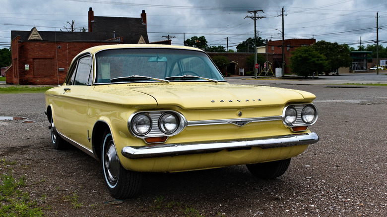 a yellow covair parked in an empty lot under a cloudy sky