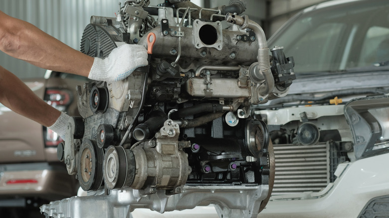 A car engine hoisted in place by an engine lift inside a shop.