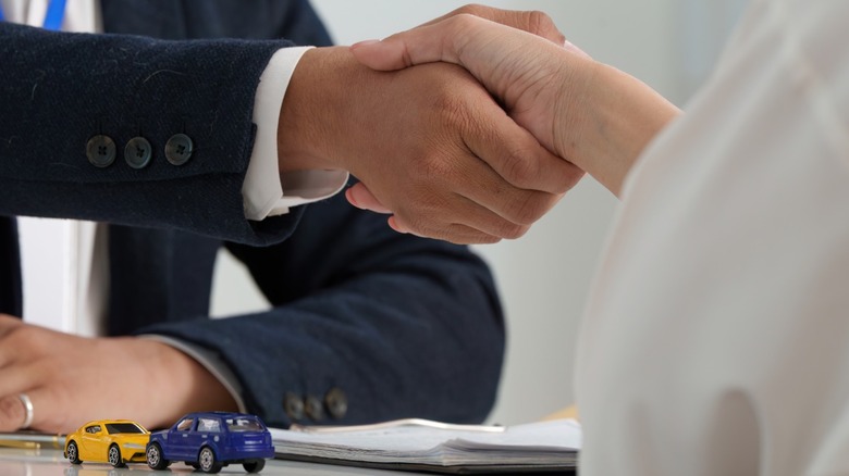 Two people shaking hands after making a deal on a car purchase.