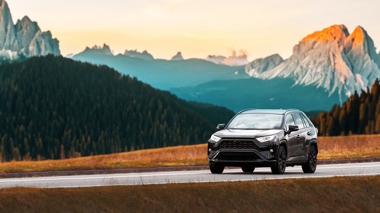 Modern family SUV car journeys along a scenic road with majestic nature and a golden sunset in the backdrop.