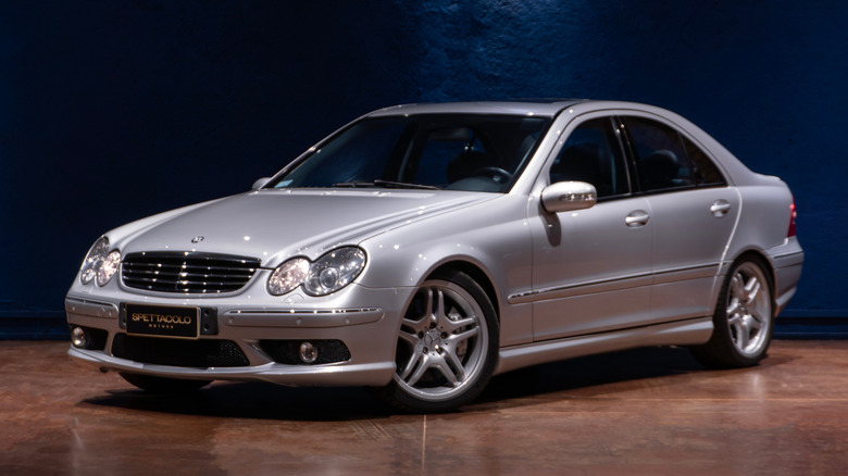 A silver W203 Mercedes-AMG C55 sitting on a brown floor in front of a blue background.