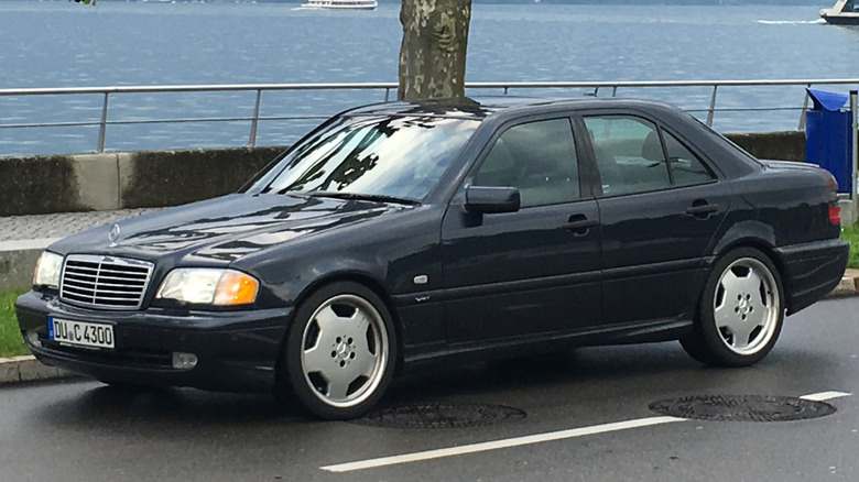 A black W202 Mercedes-AMG C43 parked on the street in front of a tree by water