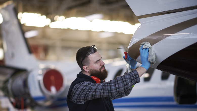 A technician wipes the exterior of a jet with a cloth and surface cleaner