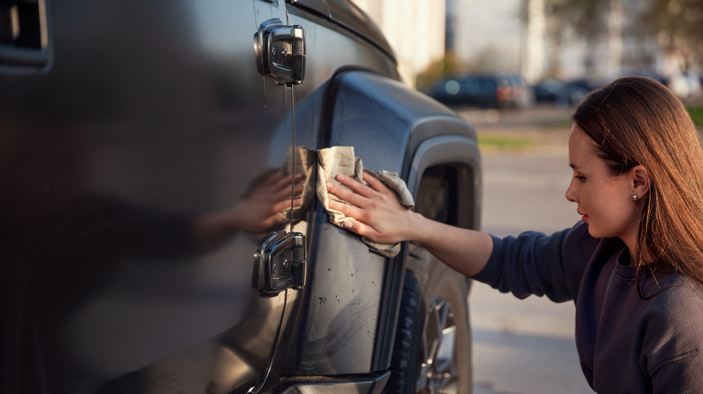 A person wiping off the excess water from a freshly washed SUV