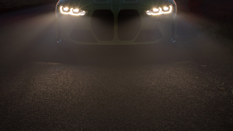 A bright yellow BMW parked on the road with its headlights on, surrounded by fog, with the sun setting in the background.