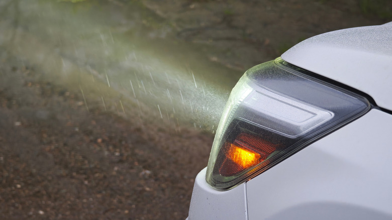 A white car with headlights on, illuminating the rain, and side reflectors activated.