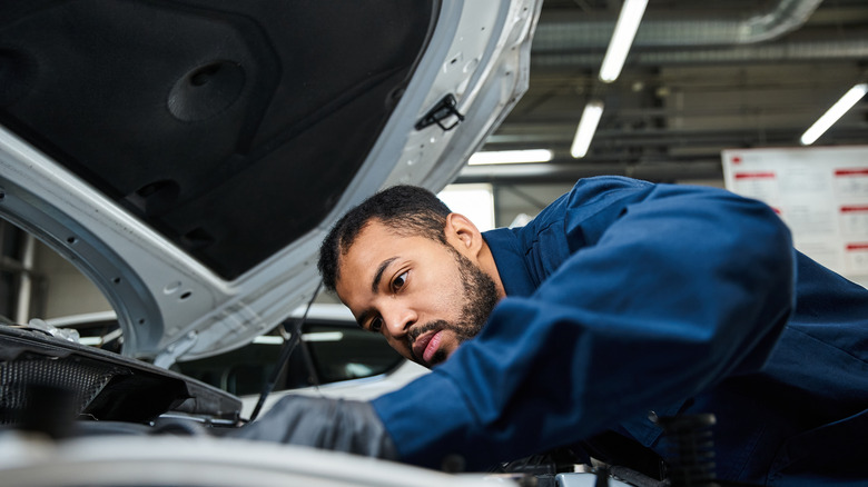 A mechanic under the hood of a car in a service center.