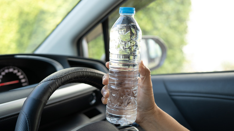 A hand holds a bottle of water inside a car