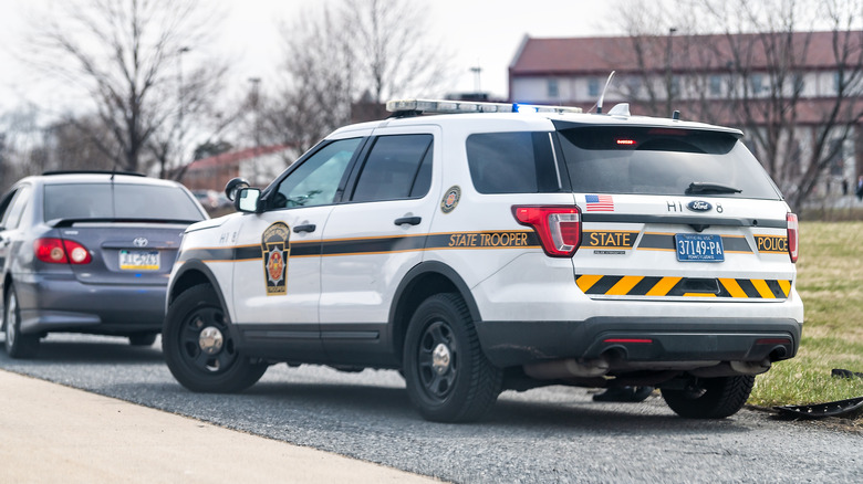 A state trooper performing a traffic stop of a gray Toyota sedan.