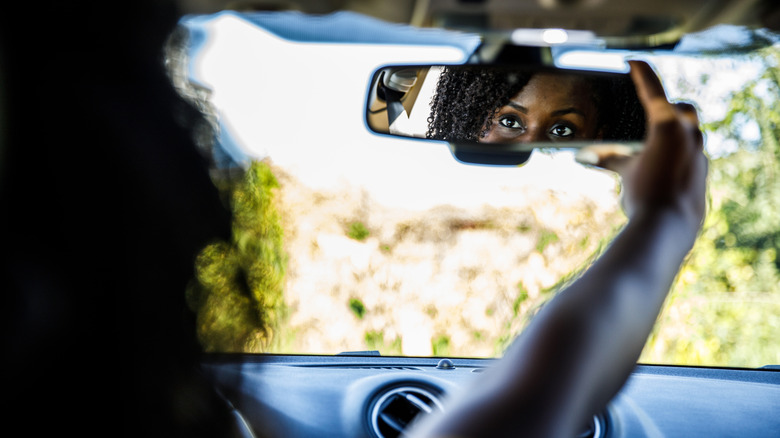 Over the shoulder view of young Black woman sitting in the driver's seat of her new car and adjusting the rear view mirror.