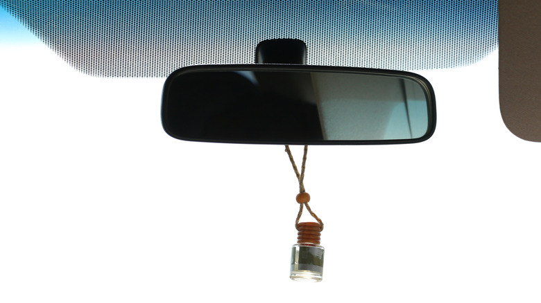 Car Rearview Mirror with Hanging Glass Air Freshener Against Clear Blue Sky Interior Driving Travel Concept