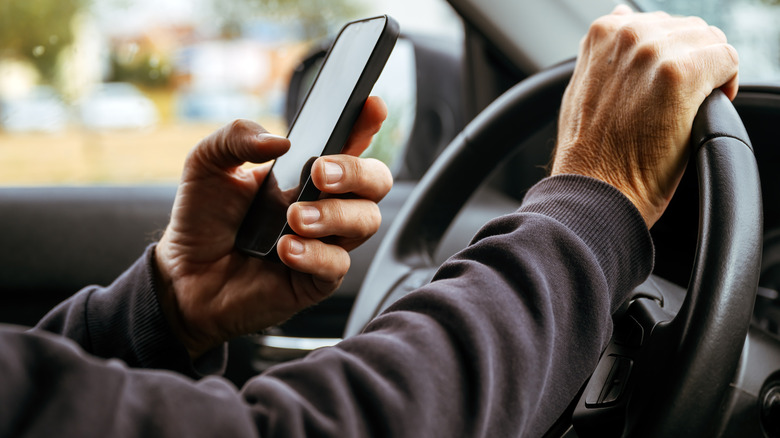 A person using a smartphone behind the wheel of a vehicle