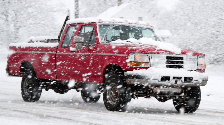 An old red pickup truck driving through a winter storm