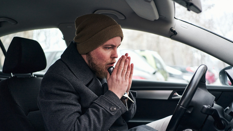 A nan trying to warm up inside a chilly car cabin