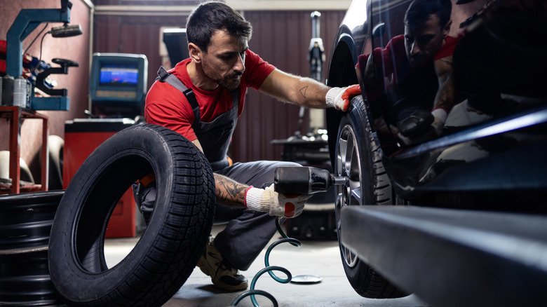 A mechanic in a shop using an impact wrench to take of a car tire.