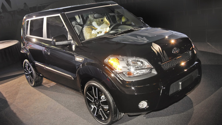 Front 3/4 of black 2010 Kia Soul being driven by a hamster at an auto show setting