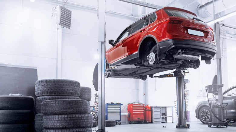 A red crossover SUV resting on a lift and waiting for new tires to be installed