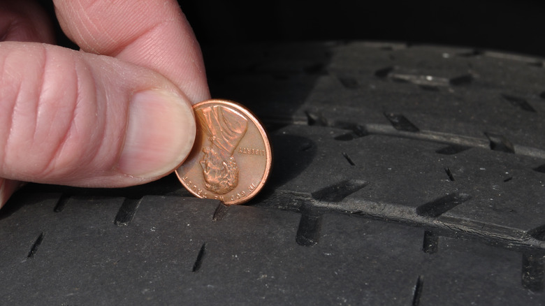 A hand holding a penny on a worn-out tire tread