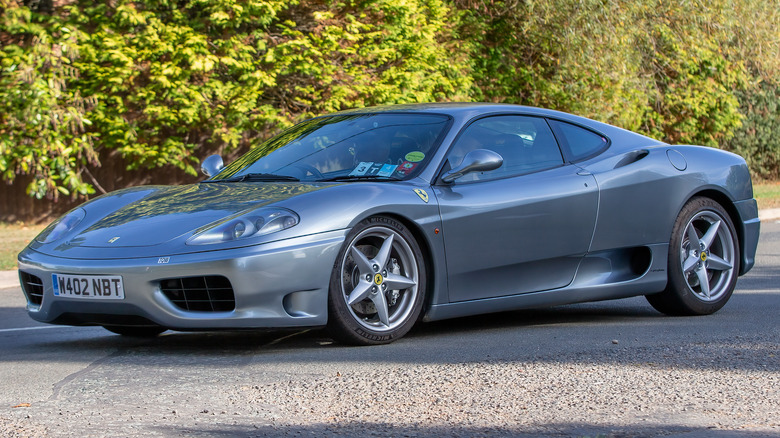 A silver-gray Ferrari 360 Modena on a road in front of trees.