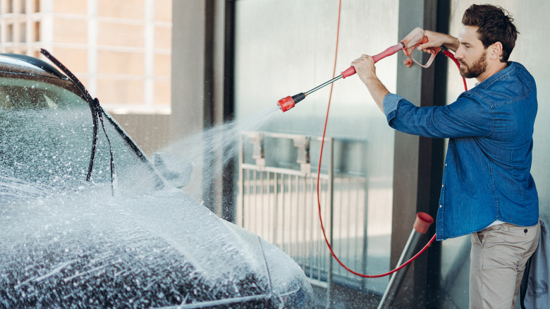 A man using a pressure washer to spray water on a car's hood.