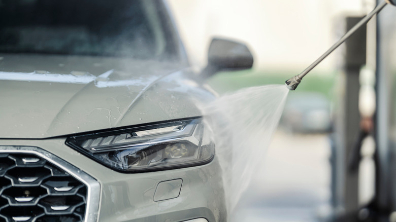 A pressure washer spraying water at the headlamp of an Audi Q5.