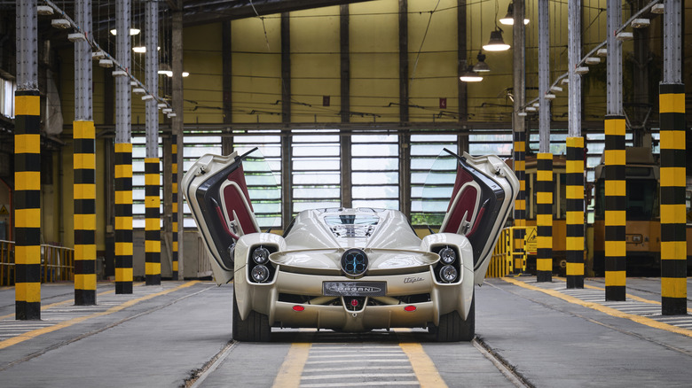 A rear shot of a tan Pagani Utopia with its doors open inside of a warehouse