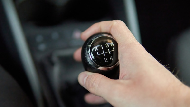 A person's hand holding a manual gear shifter inside a vehicle