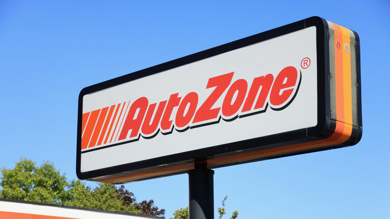 An AutoZone store sign against a blue sky with trees in the background