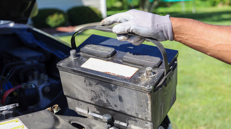 A close-up shot of a gloved hand removing an old car battery