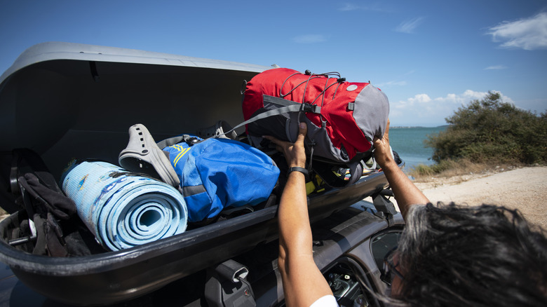 Person loading items into roof carrier.