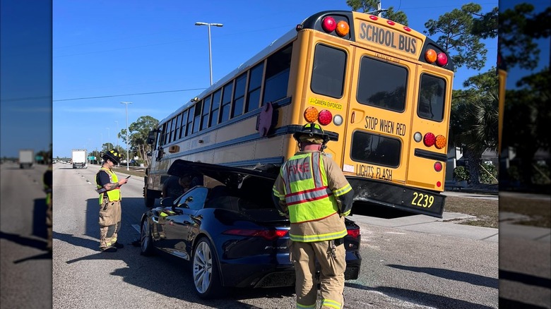 Firefighters inspect a Jaguar F-Type underneath a school bus after it crashed into the back of it