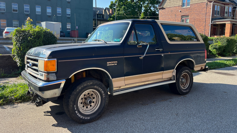 A lightly rusty Ford Bronco Eddie Bauer Edition street parked in front of buildings