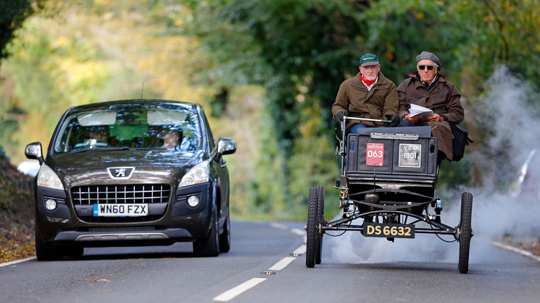 An old-timey car driving past a new one