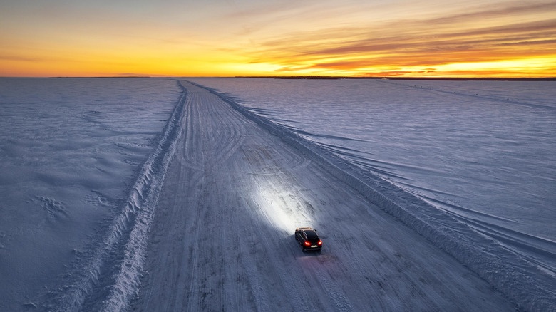 A car driving on ice with its headlights on and a sunset in the background