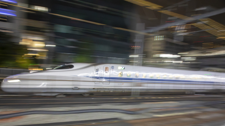 A Japanese Shinkansen bullet train streaks through an urban setting.
