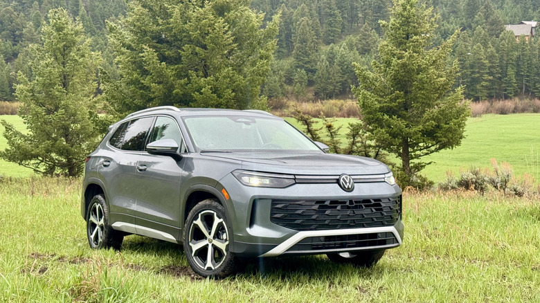 Front three quarters shot of a dark gray Volkswagen Tiguan parked on grass in front of trees and a tree-covered hill