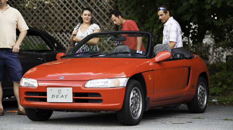 A red Honda Beat roadster with people standing near it