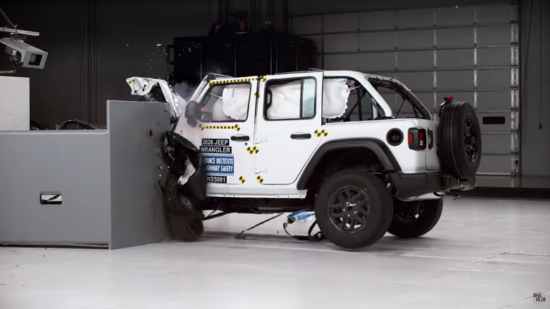 A screenshot from the IIHS video showing a side view of a white Wrangler four-door hitting the small overlap barrier with its curtain airbags deployed